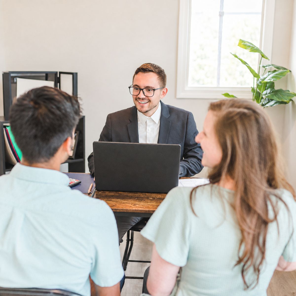 An advisor goes over customer details on a laptop with two clients in a bright office